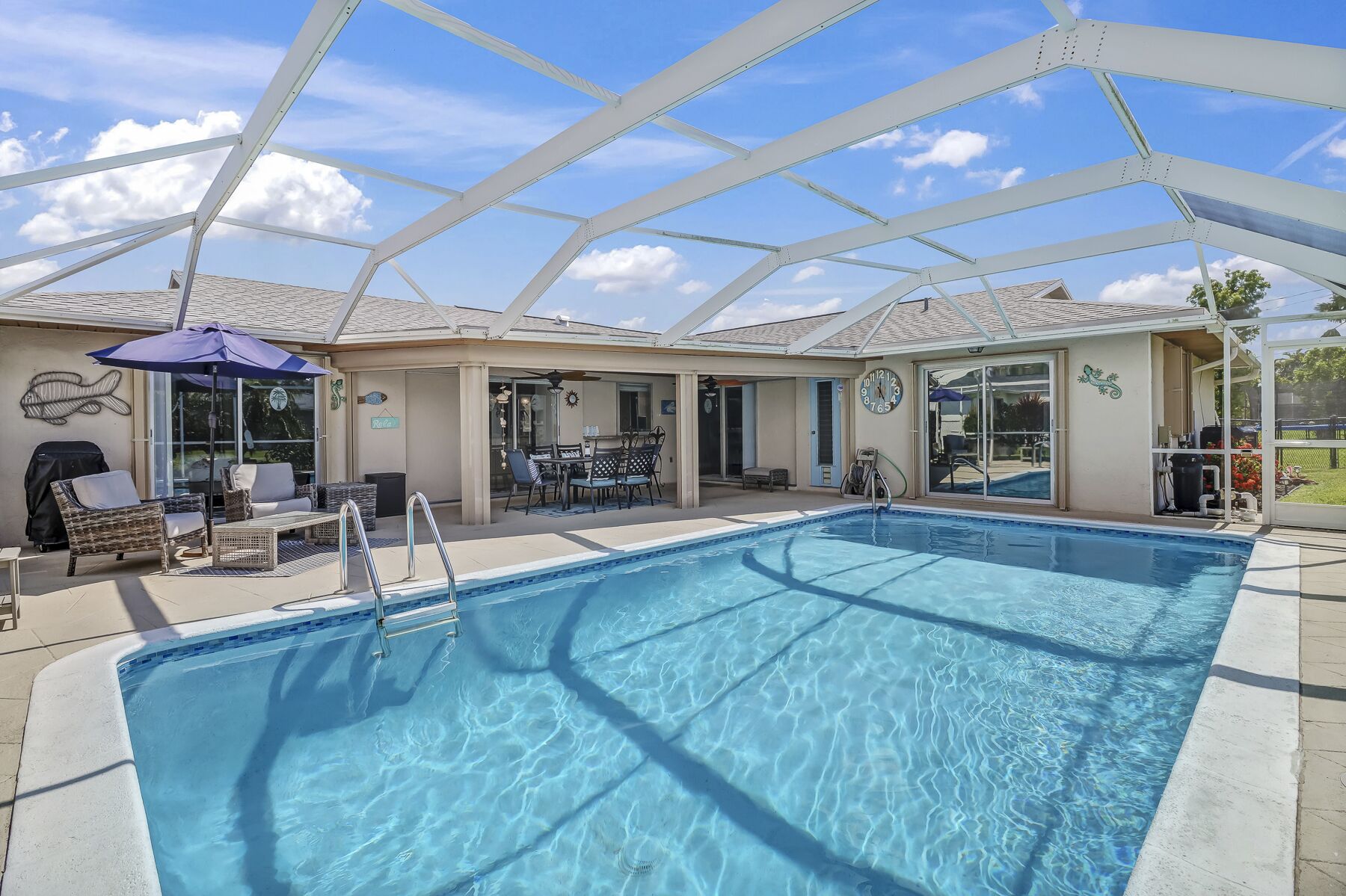 A swimming pool with a covered patio area, outdoor furniture, and a grill.