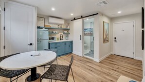 A modern kitchen with blue cabinets, a white dining table, and a glass-enclosed shower area. - Coastal hideaway w/ beach access & workspace (San Clemente)