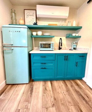 Compact kitchen with a microwave, coffee maker, and refrigerator, offering a well-organized space with a framed quote.