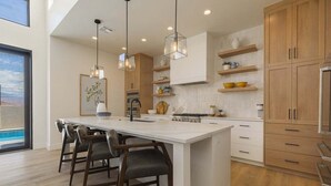 Cocina moderna con una isla grande, luces colgantes, armarios de madera y vistas al exterior.