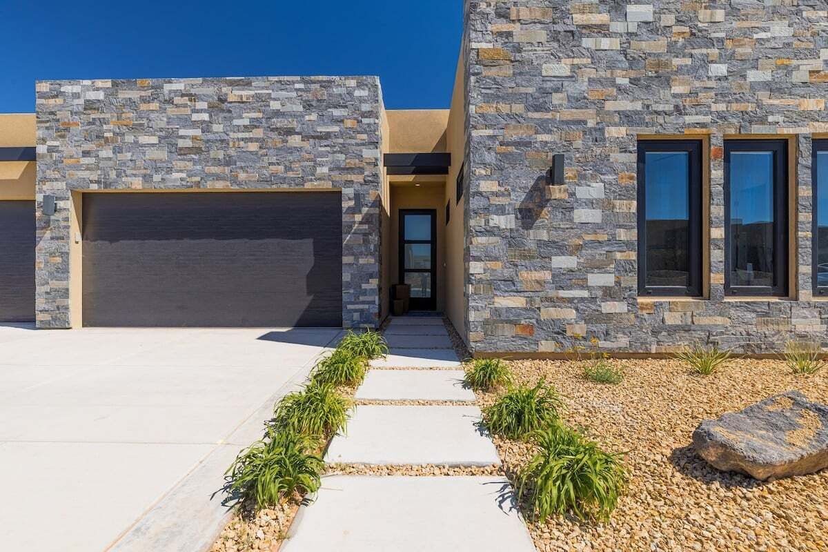 A modern house with a stone facade, a garage, and a pathway leading to the entrance.