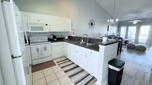 A modern kitchen with white cabinets, a microwave, stove, and granite countertops. There is a black trash bin and a striped rug on the floor.