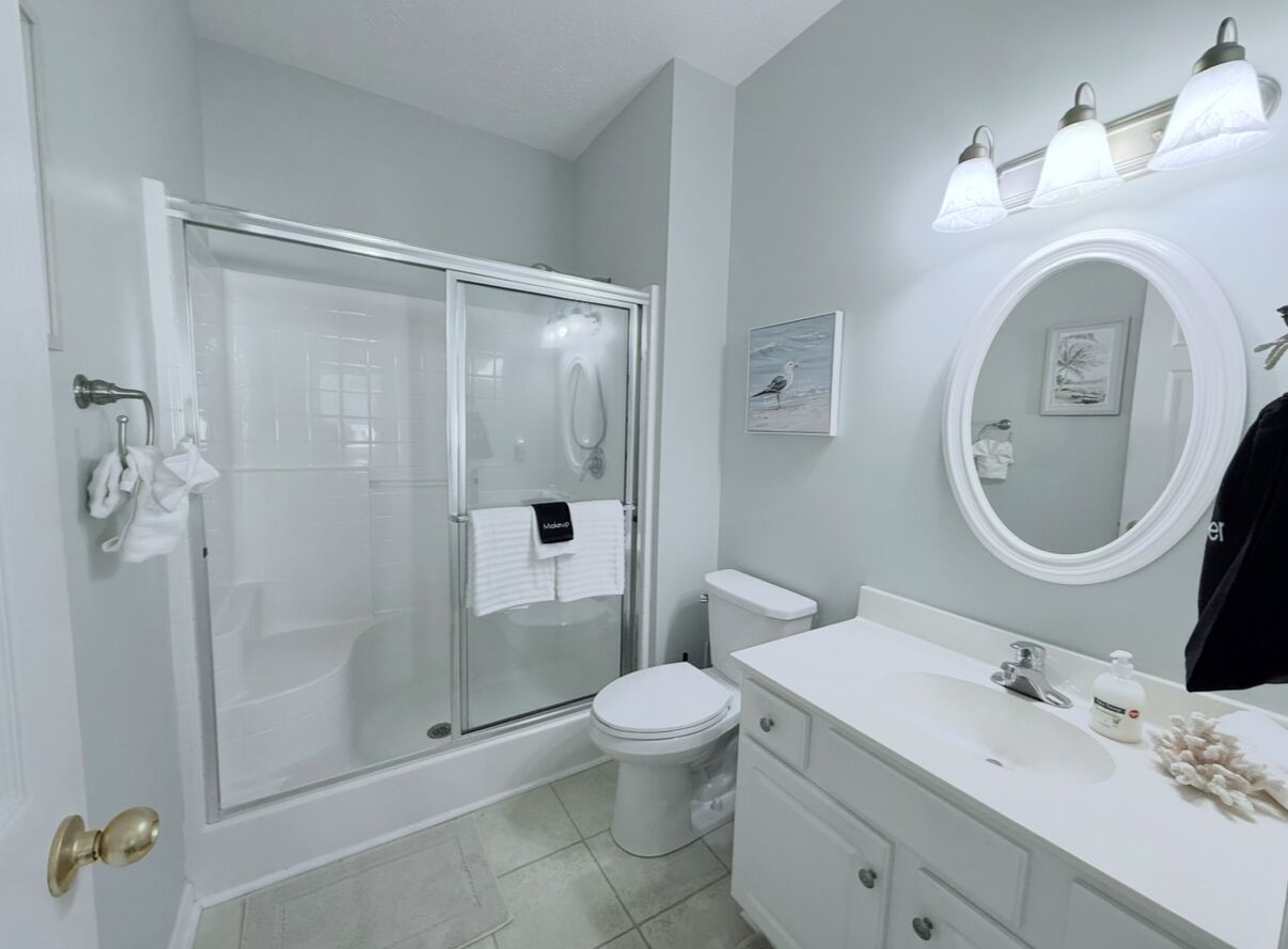 Une salle de bain avec une douche à parois de verre, des toilettes, un lavabo avec un miroir et un porte-serviettes.