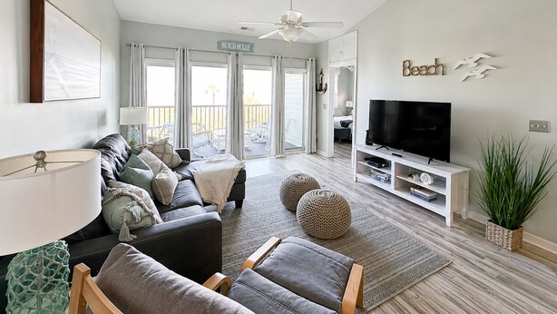 A modern living room with a sofa, TV, and a balcony with a sign reading 'Beach House'.