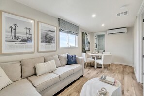 Un salon moderne avec un canapé beige, une table à manger avec des chaises et une petite table blanche sur laquelle se trouve un livre.
