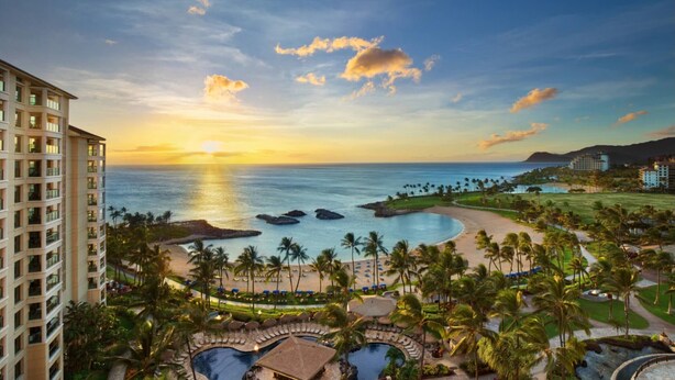 Un resort con piscina, palmeras y vistas al océano al atardecer.