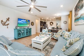 A living room with a ceiling fan, a TV, a dining area, and a kitchen.