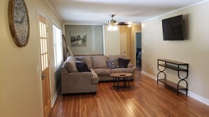 Una sala de estar con un sofá modular, una mesita redonda y un televisor montado en la pared.