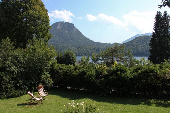 Un espacio cubierto de hierba con una silla de madera y un lago con montañas al fondo.