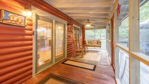 Une cabane en rondins dotée d’un porche en bois, de portes-fenêtres coulissantes et d’un ventilateur de plafond.