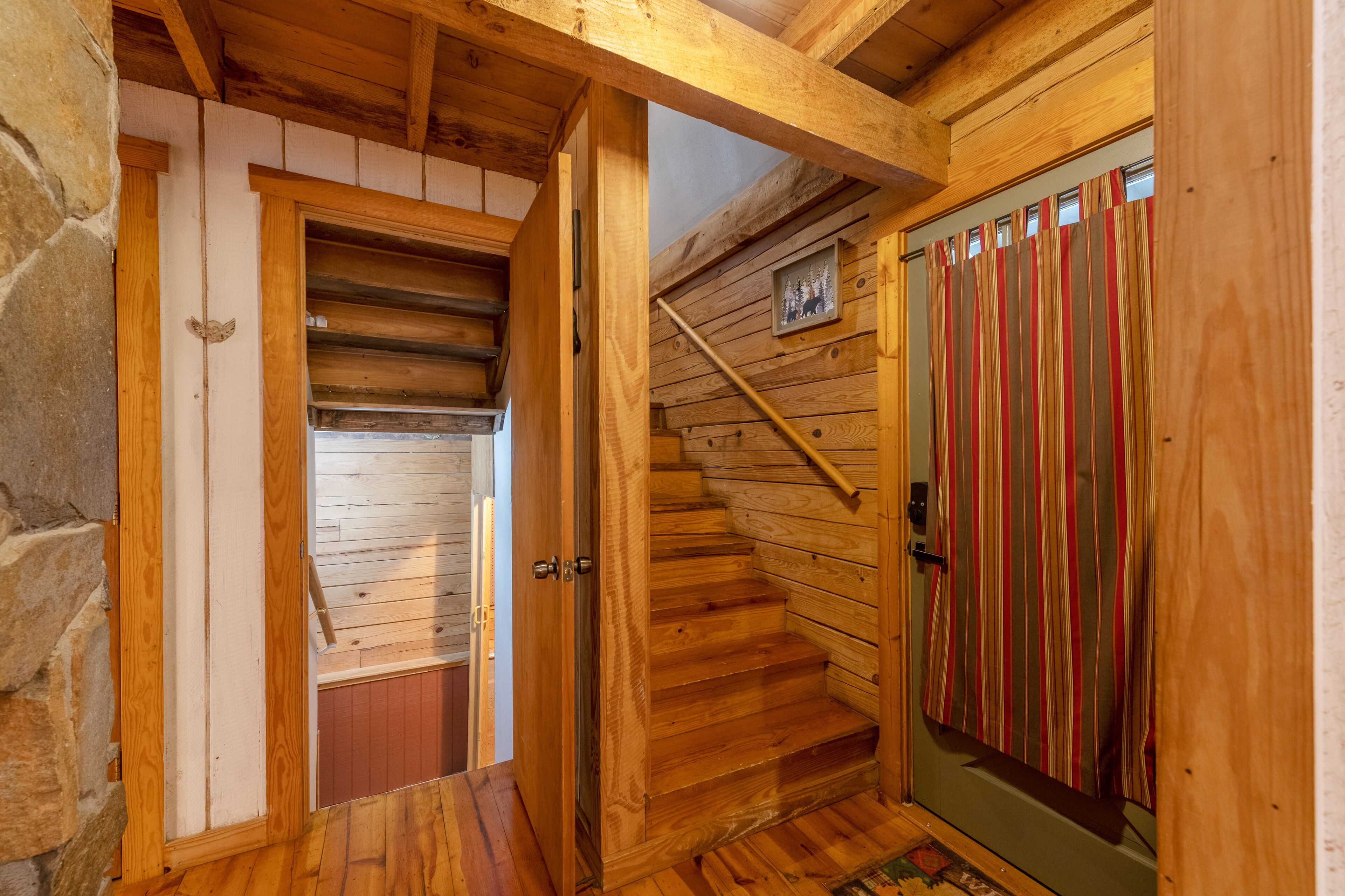 Una escalera de madera que lleva a una habitación con una cortina a rayas y un cuadro pequeño en la pared.