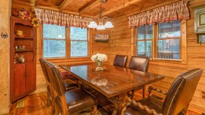 L’intérieur d’un chalet en bois comprend une table à manger, des chaises, un buffet et un lustre.