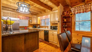 Une cuisine de style rustique, avec des éléments en bois, comprenant un îlot central, des placards en bois, un four à micro-ondes encastré et un coin repas avec une table et des chaises.