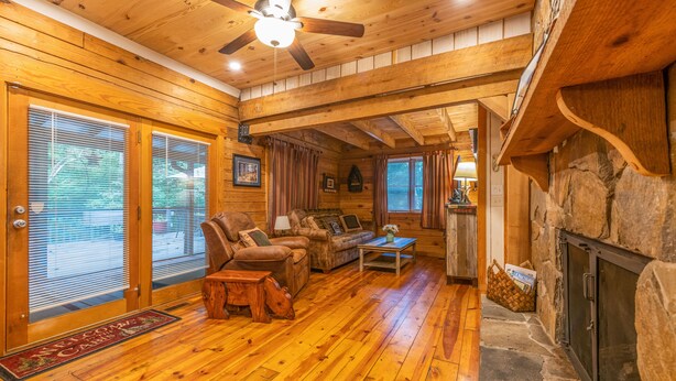 L’intérieur d’une cabane en rondins, avec un plancher en bois, une cheminée, un ventilateur de plafond et un mur en pierre.