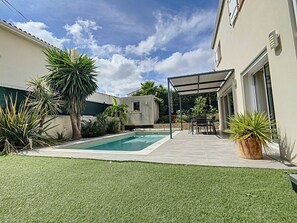 Un patio trasero con piscina, un porche cubierto y diversas plantas.
