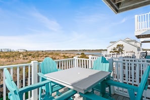 A balcony with a white table and turquoise chairs, overlooking a beach and a white building.