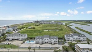 A coastal residential area with multiple apartment buildings, a swimming pool, and a view of the ocean. - Cozy 2BR - 2BA Condo - Ocean, Marsh & ICW Views • Pool & Private Dock • Sleeps 6 (Ocean Isle Beach)