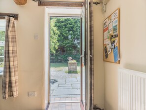 An open door leading to a garden with a wooden fence, a bulletin board with various notices, and a power outlet on the wall. - Primrose Cottage - UKC6679 (Betws Yn Rhos)
