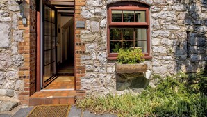 A stone building with a wooden door and a window with a planter. - Primrose Cottage - UKC6679 (Betws Yn Rhos)
