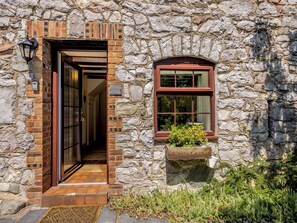 A stone building with a wooden door and a window with a planter. - Primrose Cottage - UKC6679 (Betws Yn Rhos)
