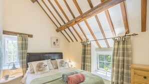 A cozy bedroom with a bed, a nightstand, a lamp, and a window with curtains. - Primrose Cottage - UKC6679 (Betws Yn Rhos)