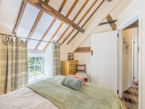 A bedroom with a sloped ceiling, a bed with a green blanket, a wooden dresser, and a view of the outdoors through a window.