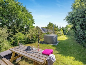 A wooden picnic table with a bottle, glasses, and a hat. A hot tub is visible in the background. - Primrose Cottage - UKC6679 (Betws Yn Rhos)