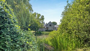 A stone house with a pond in front, surrounded by lush greenery. - Primrose Cottage - UKC6679 (Betws Yn Rhos)