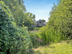 A stone house with a pond in front, surrounded by lush greenery. - Primrose Cottage - UKC6679 (Betws Yn Rhos)
