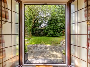 A view through a glass door with a stone pathway leading to a green garden area. - Lavender Cottage - UKC6677 (Betws Yn Rhos)