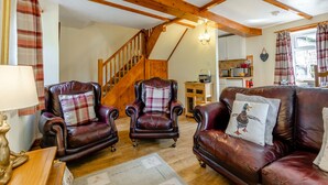 A cozy living room with leather armchairs, a wooden staircase, and a kitchen in the background. - Lavender Cottage - UKC6677 (Betws Yn Rhos)