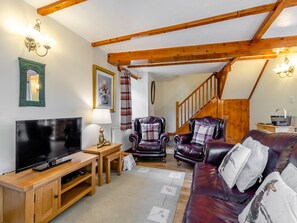A cozy living room with a wooden TV stand, leather sofas, and a staircase. - Lavender Cottage - UKC6677 (Betws Yn Rhos)