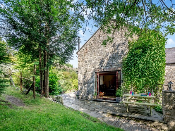 A stone building with a wooden door, a picnic table with chairs, and a stone pathway leading to the entrance.