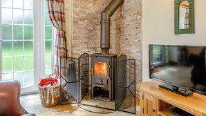 A cozy room with a stone wall, a fireplace, a television, and a wicker basket. - Lavender Cottage - UKC6677 (Betws Yn Rhos)