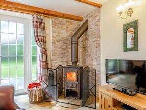 A cozy room with a stone wall, a fireplace, a television, and a wicker basket. - Lavender Cottage - UKC6677 (Betws Yn Rhos)