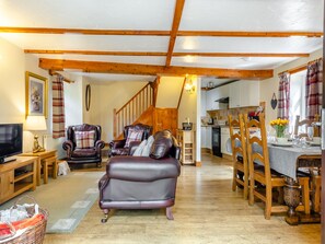 A spacious living room with a leather sofa, wooden chairs, a TV, and a dining area with a table set for two. - Lavender Cottage - UKC6677 (Betws Yn Rhos)