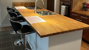 Een moderne keuken met een houten eiland, roestvrijstalen apparatuur en hangende lampen.