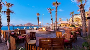 An outdoor seating area with wooden chairs and tables, a fire pit, and a view of the sea and mountains. - Villa Del Palmar Cabo San Lucas Junior Suite /w Kitchen & View (Cabo San Lucas)