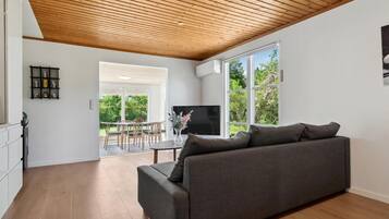A modern living room with a grey sofa, wooden flooring, and a wooden ceiling.