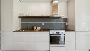 Ett modernt kök med vita skåp, en köksfläkt i rostfritt stål och en kakelbeklädd vägg bakom arbetsbänken.