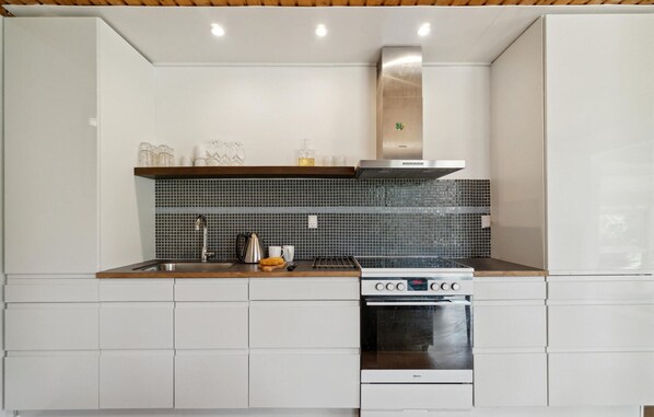 Een moderne keuken met witte kasten, een roestvrijstalen afzuigkap en een betegelde achterwand.