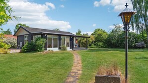 Ett modernt hus med en täckt veranda, en stensatt gång som leder till entrén och en gräsmatta med en lyktstolpe.
