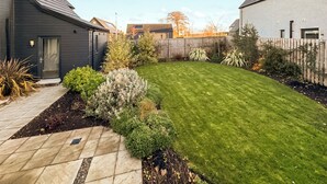 A residential backyard with a well-maintained lawn, a wooden deck, and a variety of shrubs and plants. - 3 bedroom accommodation in Croy, near Inverness (Croy, near Inverness)