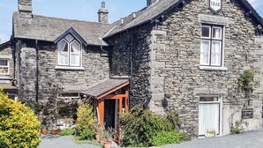 A stone building with a traditional architectural style, featuring a prominent chimney, a date plaque reading "A.D. 1858", and a small porch area.