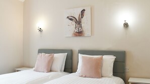 A bedroom with two beds, each with a grey headboard and white bedding. There is a wall-mounted painting of a rabbit above the beds.