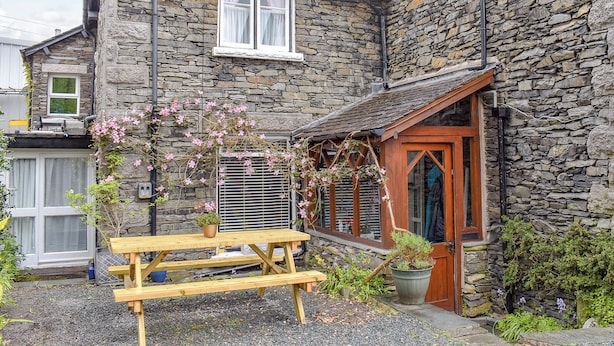 A stone building with a wooden door, a window with curtains, and a wooden bench in the foreground.