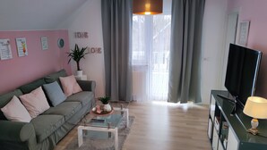 Un salon avec un canapé vert, une table basse, un téléviseur et une fenêtre avec des rideaux.