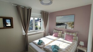 Une chambre à coucher avec un lit, une fenêtre avec des rideaux, un tableau au mur et une table de chevet avec une lampe.