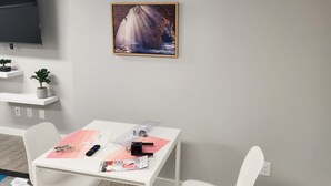 A modern room with a white table, two white chairs, a mounted TV, a framed picture of a waterfall, and a small potted plant. - Spacious Basement Suite in Bonavista With Separate Entrance (Winnipeg)
