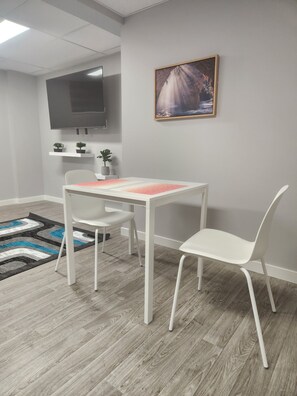 A modern room with a white table and chairs, a mounted TV, a painting, and a patterned rug.